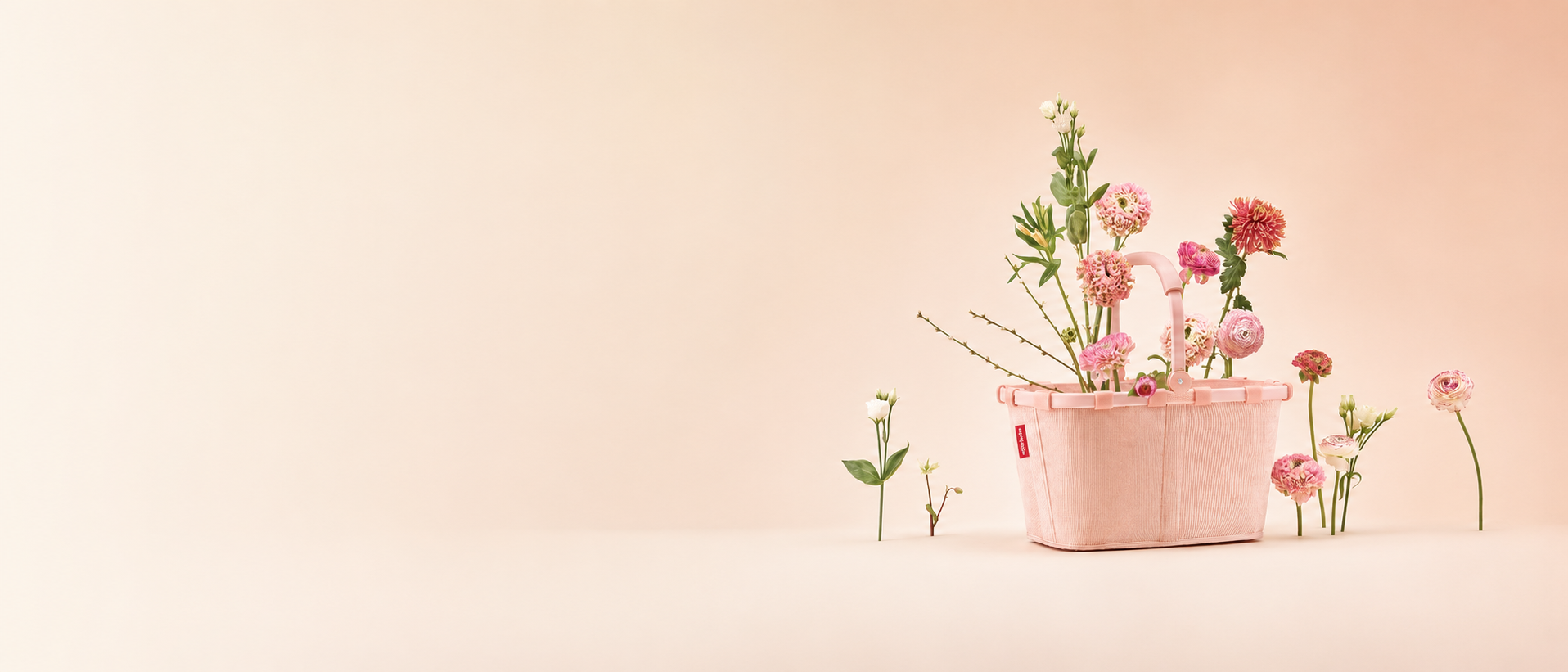 Rosafarbene Reisenthel Tasche mit Blumenarrangement auf pastellrosa Hintergrund.