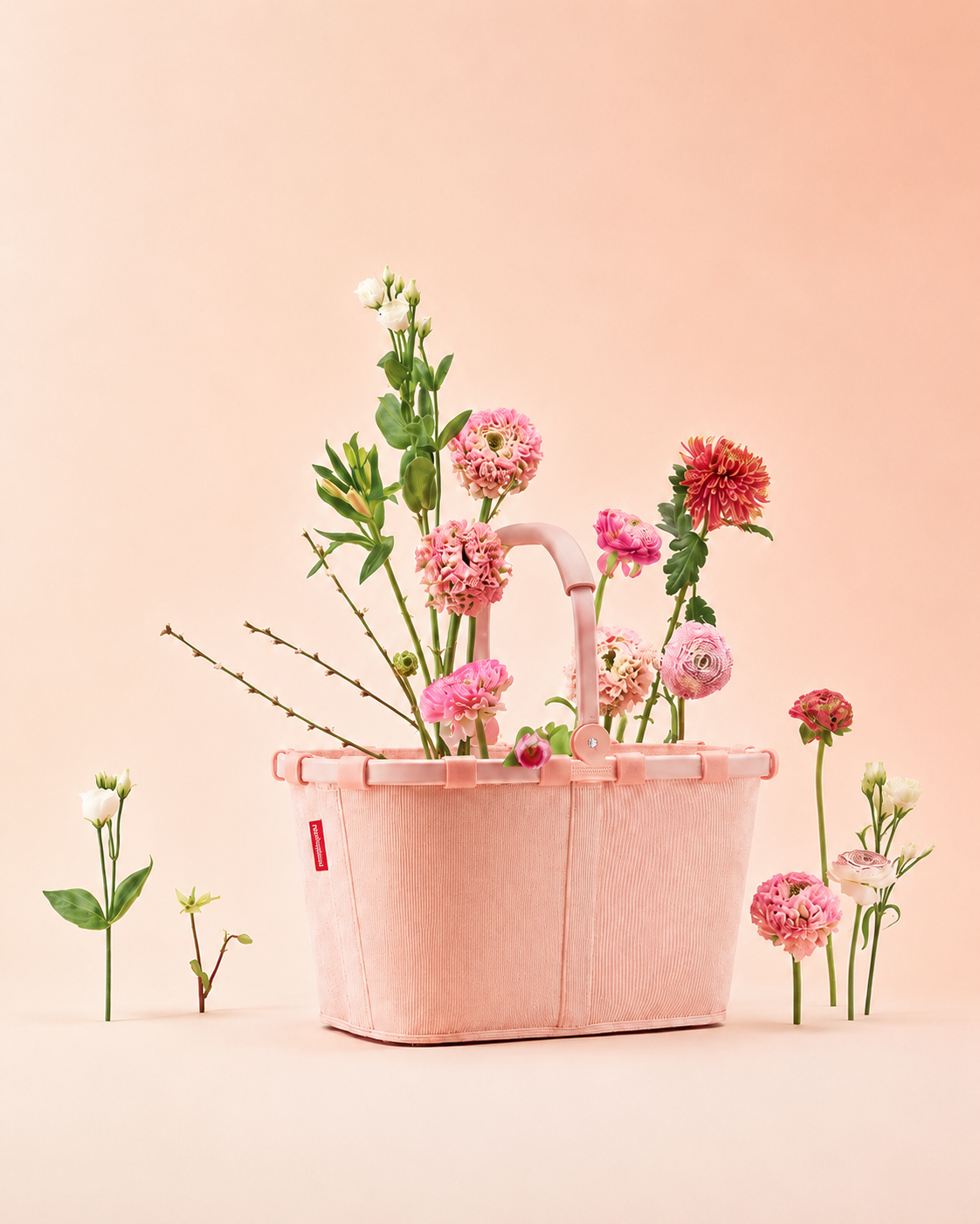 Rosafarbene Reisenthel Tasche mit Blumenarrangement auf pastellrosa Hintergrund.